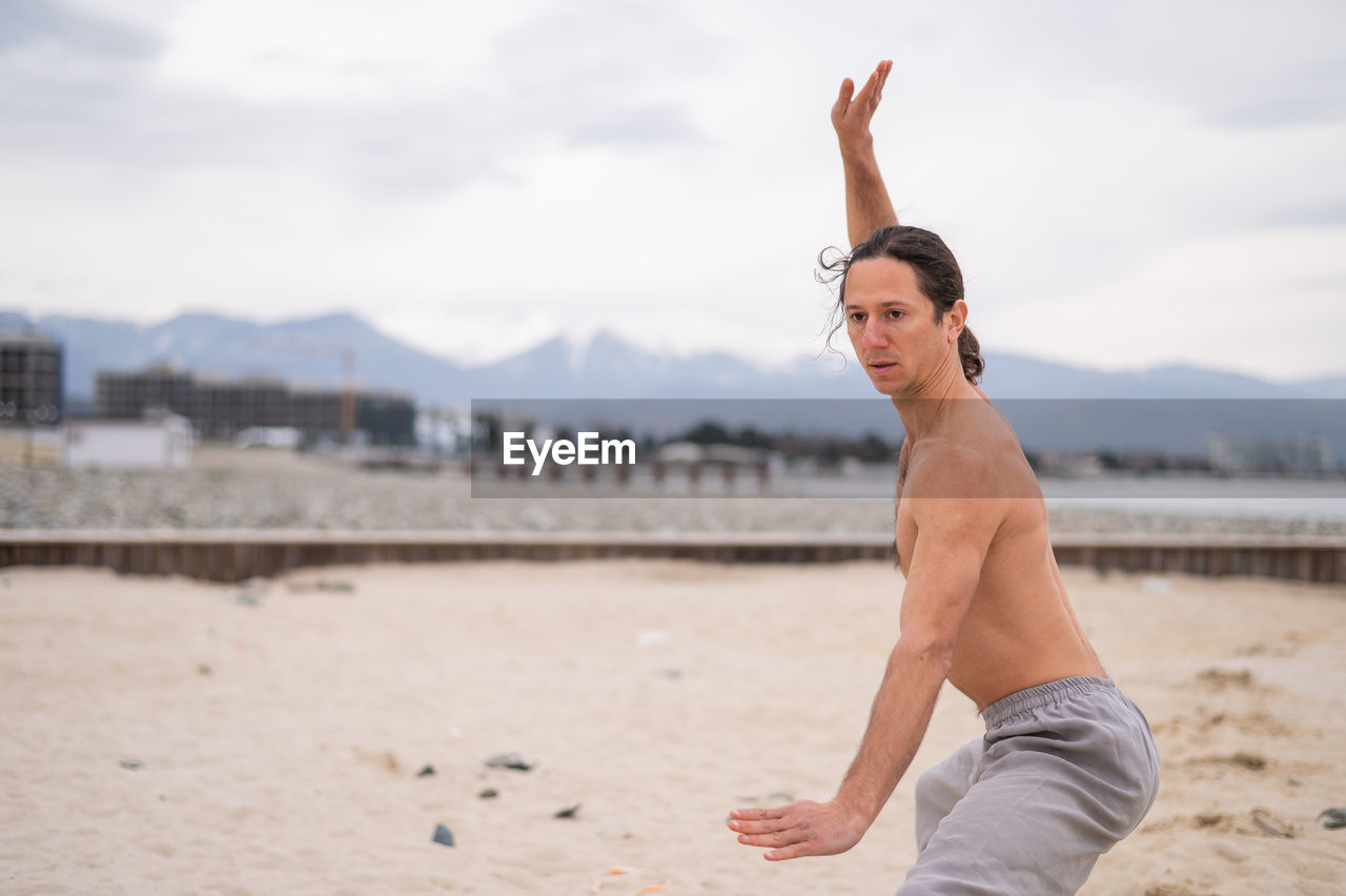 full length of young woman exercising at beach against sky