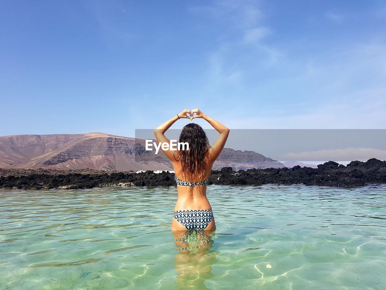 Rear view of seductive woman posing while standing in sea