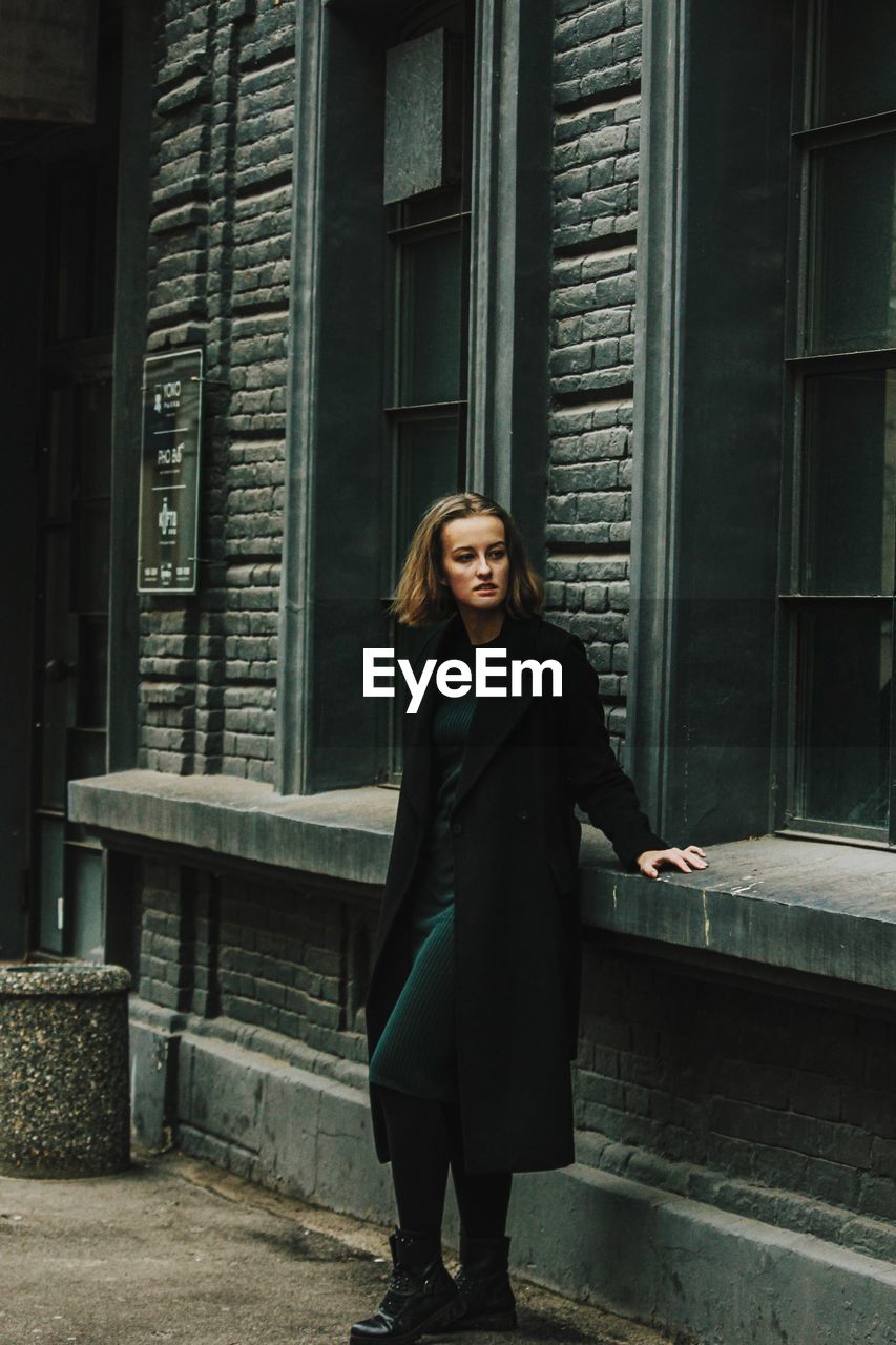 Full length portrait of woman standing against building