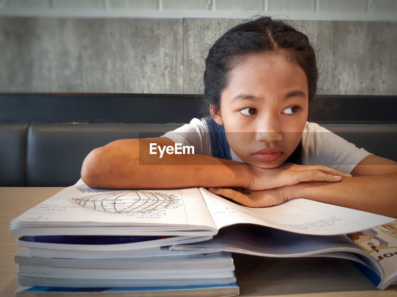 Girl with hand on chin looking away while studying at home