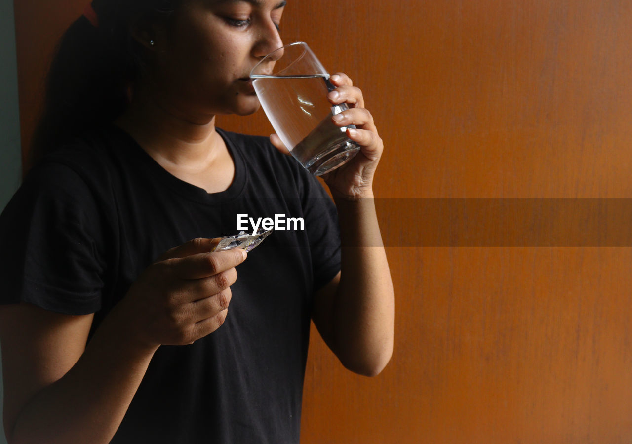 Midsection of young woman drinking water standing at home