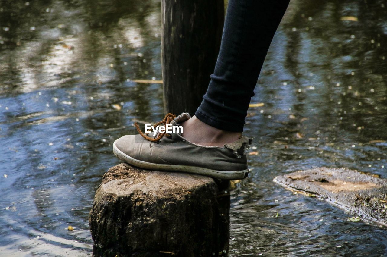 Low section of person wearing old shoe standing by lake