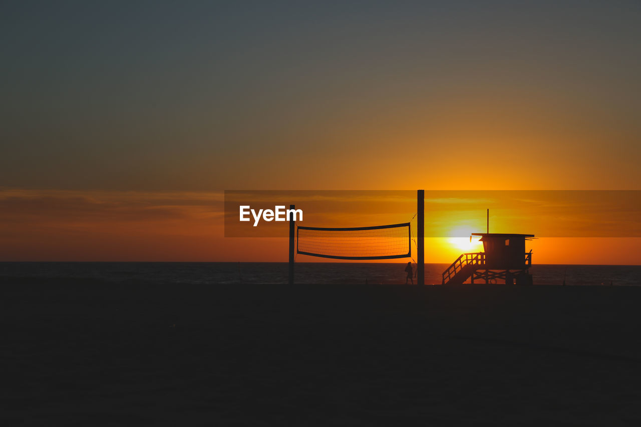 SILHOUETTE BEACH BY SEA AGAINST ORANGE SKY