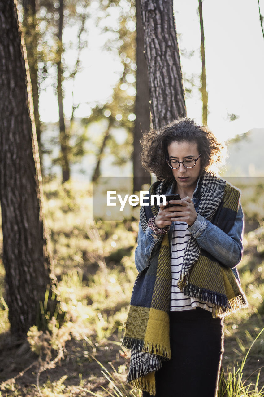 Woman using phone while standing in forest