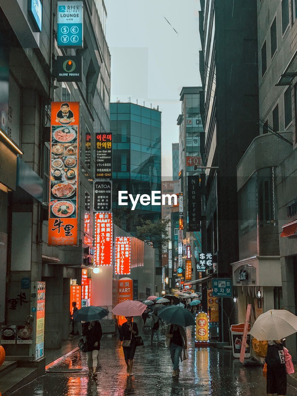 People walking on wet street amidst buildings in city