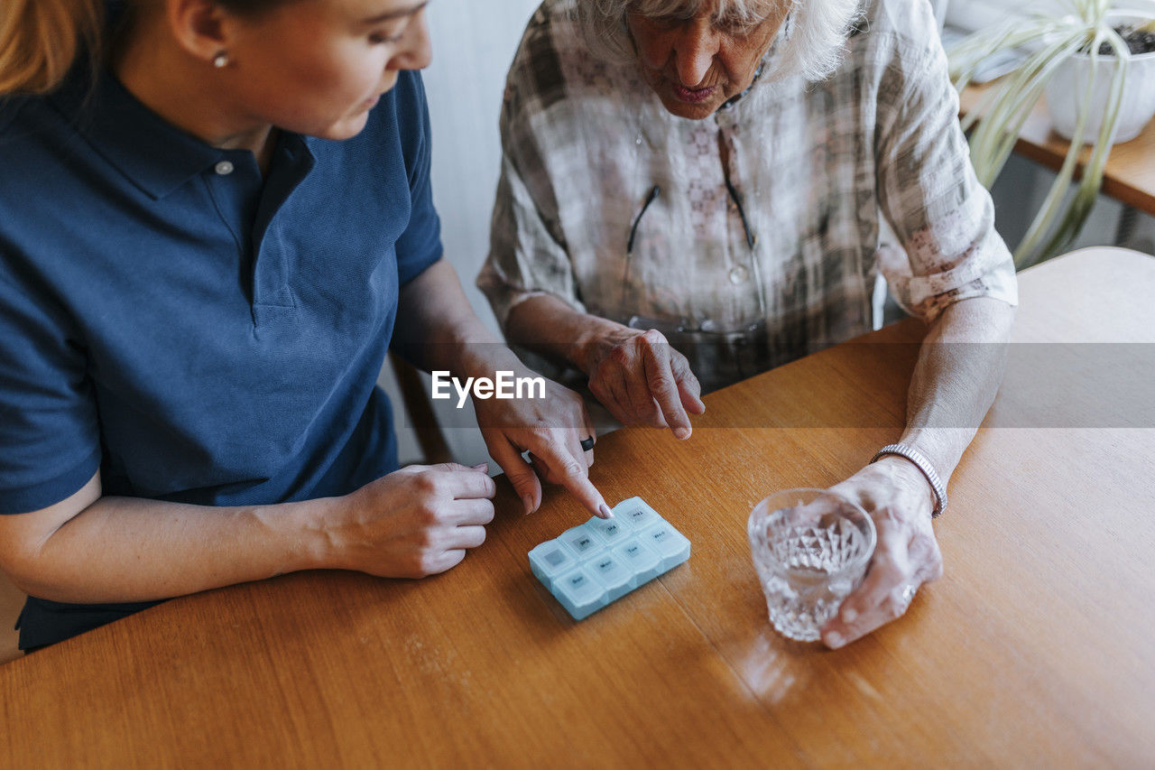 High angle view of female caregiver explaining dose of medicines to senior woman at home