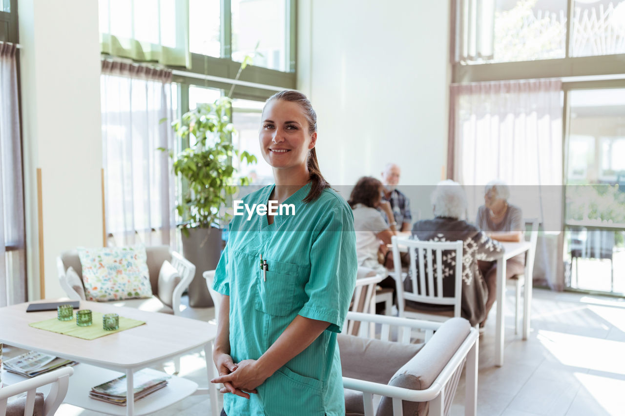 Portrait of smiling female healthcare worker with senior people in background at nursing home