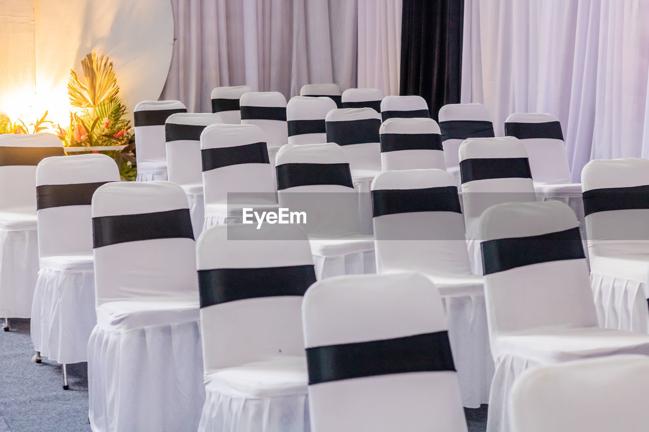 seat, chair, function hall, banquet, furniture, table, meal, event, indoors, white, empty, no people, in a row, curtain, room, celebration, business, interior design, conference hall, absence