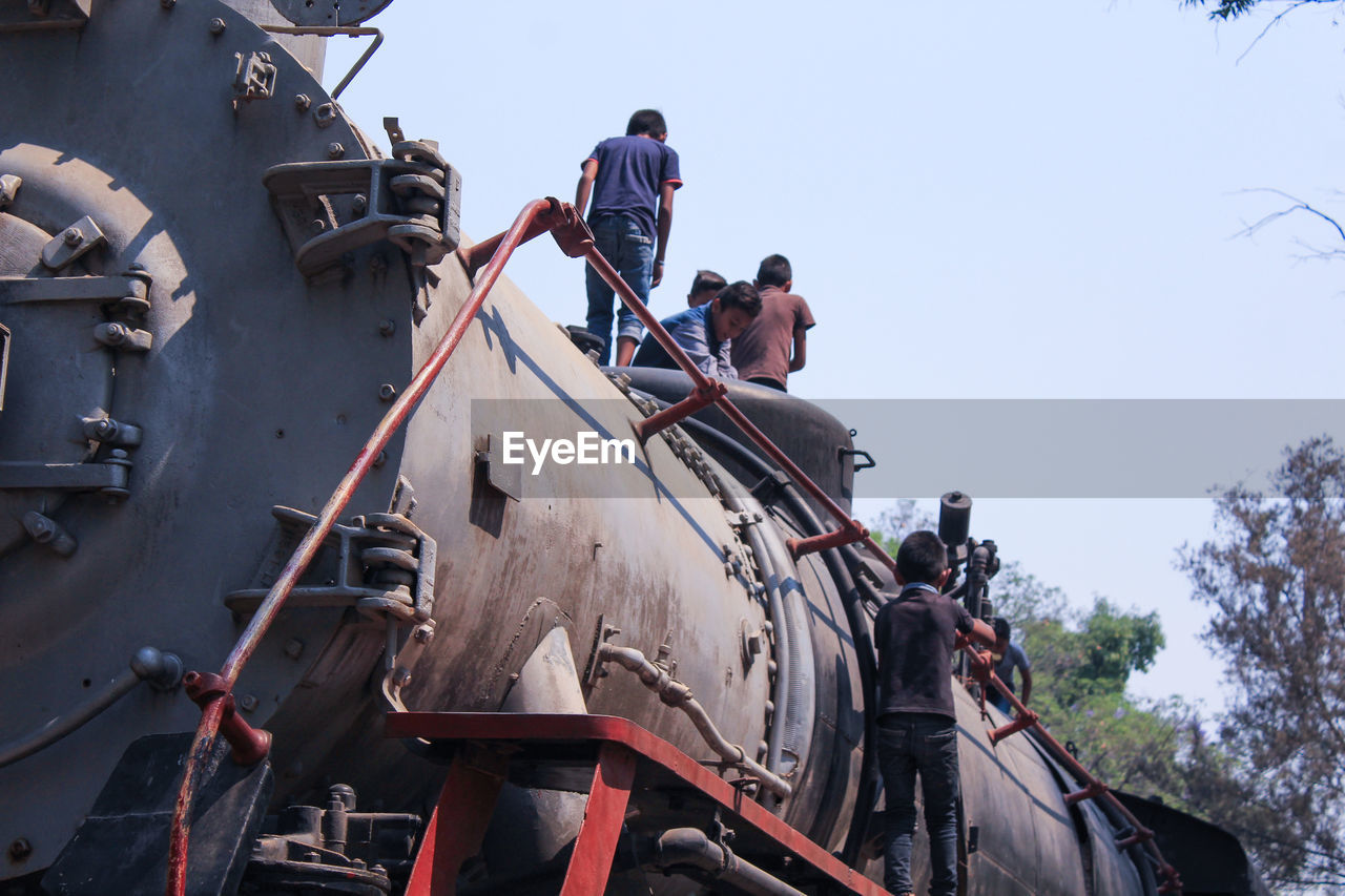 Low angle view of boys climbing freight train against clear sky