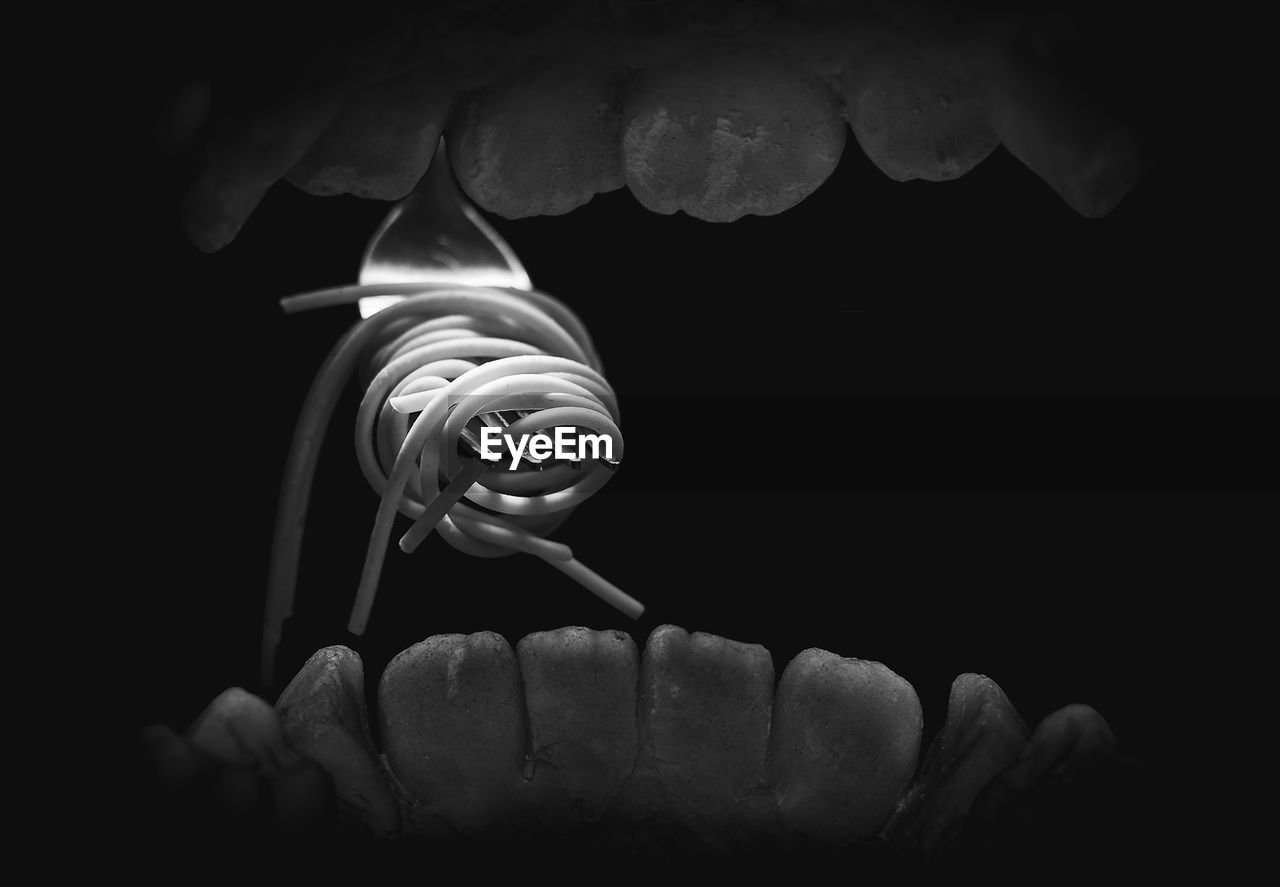 Noodles and fork in human mouth against black background