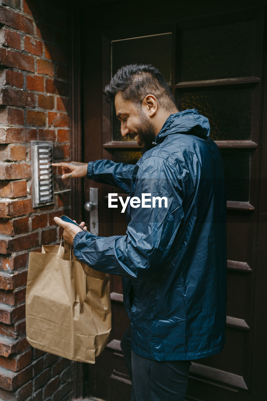 Smiling male food delivery person ringing doorbell while standing outside house