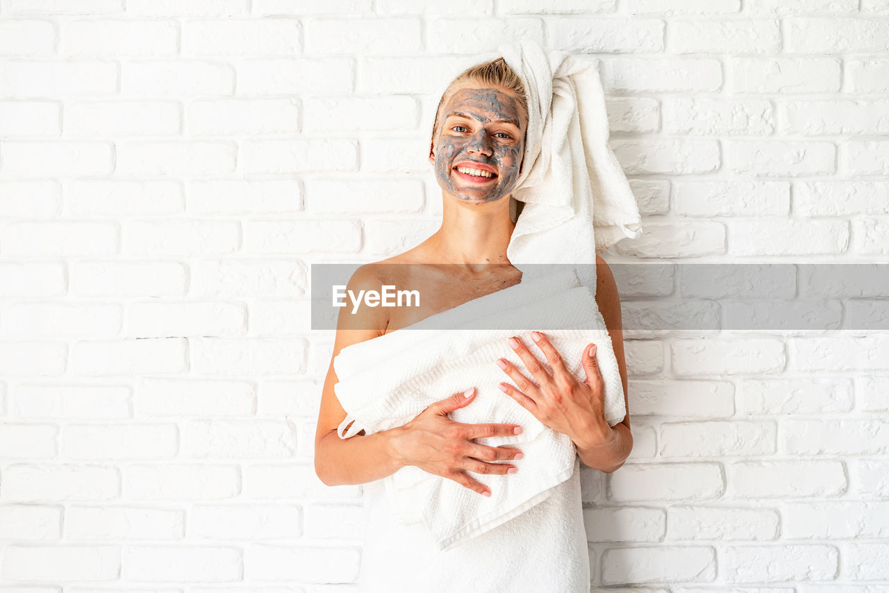 Spa and beauty. young smiling woman holding white bath towels with a clay facial mask on her face