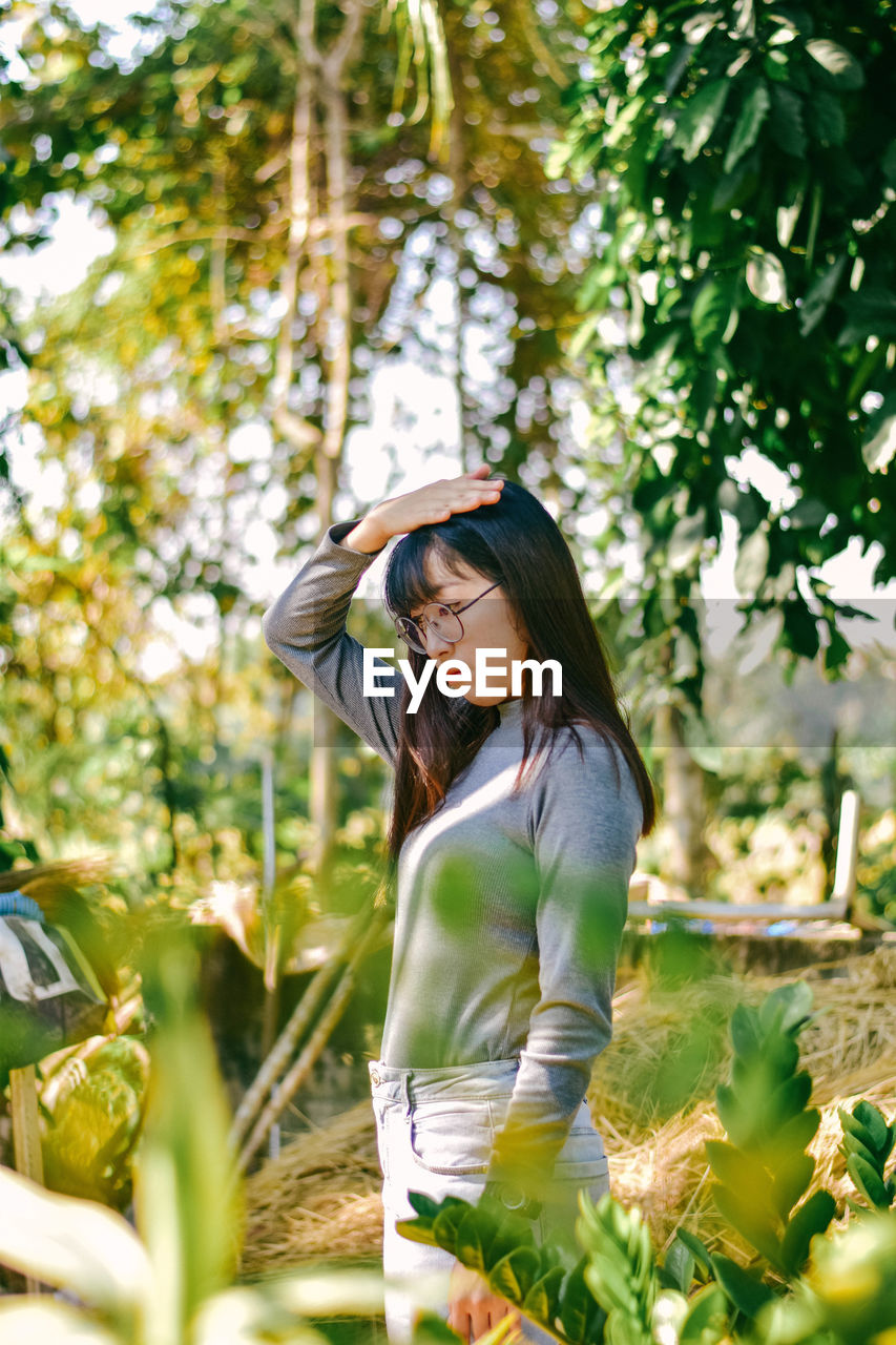 Thoughtful young woman standing against trees