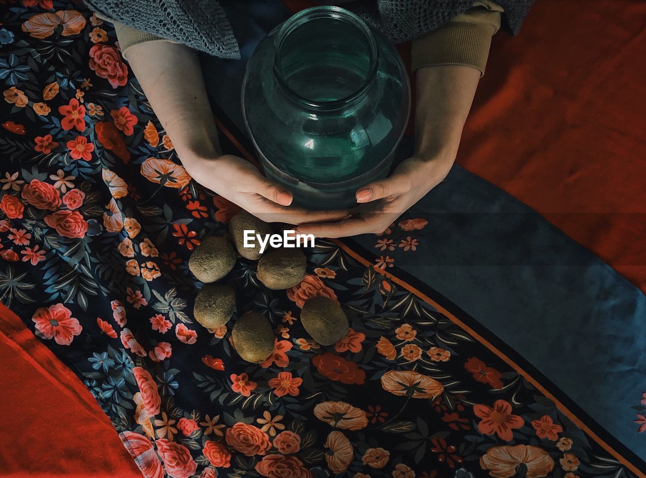 Cropped hand of woman holding container with kiwi on floor