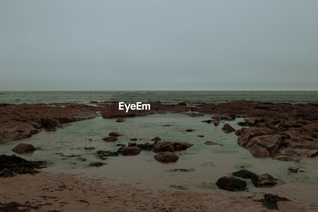 sea, water, land, sky, beach, horizon over water, body of water, ocean, horizon, rock, nature, scenics - nature, beauty in nature, shore, coast, wave, tranquility, sand, environment, tranquil scene, no people, natural environment, bay, morning, coastline, seascape, wind wave, outdoors, landscape, clear sky, travel destinations, day, copy space, non-urban scene, idyllic
