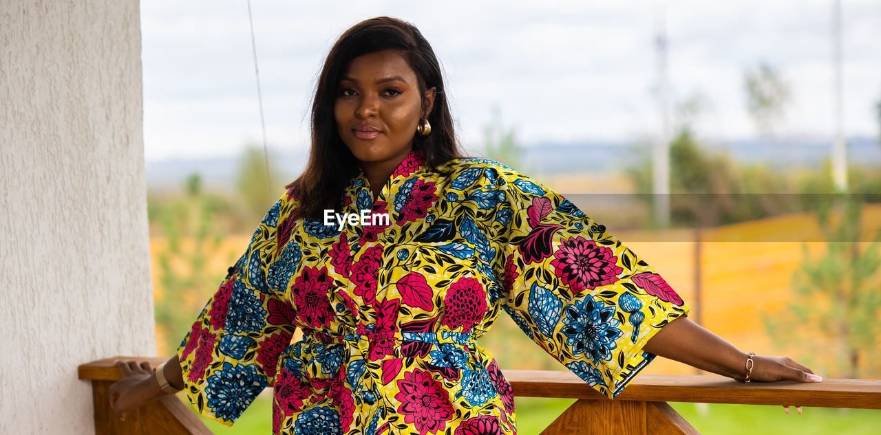 one person, adult, spring, women, portrait, yellow, smiling, looking at camera, clothing, dress, standing, photo shoot, young adult, lifestyles, happiness, hairstyle, waist up, nature, three quarter length, front view, female, emotion, day, outdoors, floral pattern, person, focus on foreground, pattern, traditional clothing, relaxation, architecture, leisure activity, fashion, multi colored, black hair, long hair, casual clothing, cheerful