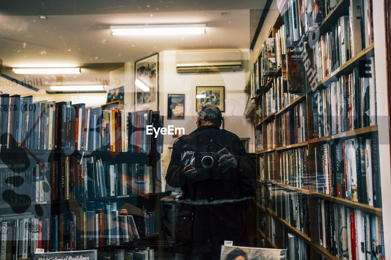 shelf, indoors, building, library, person, clothing, store, bookshelf, one person, adult, publication, book, architecture, bookcase, occupation, room