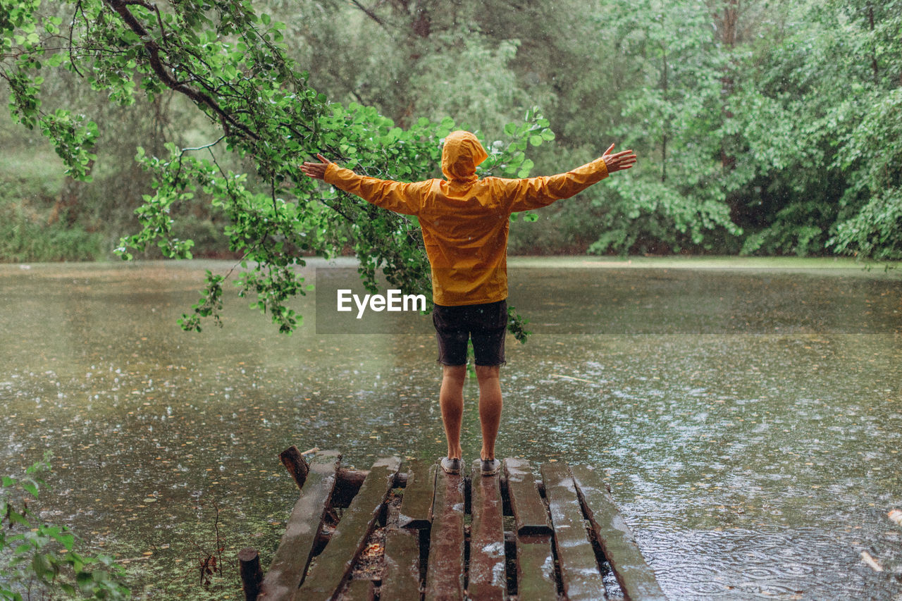 REAR VIEW OF MAN STANDING BY CALM LAKE