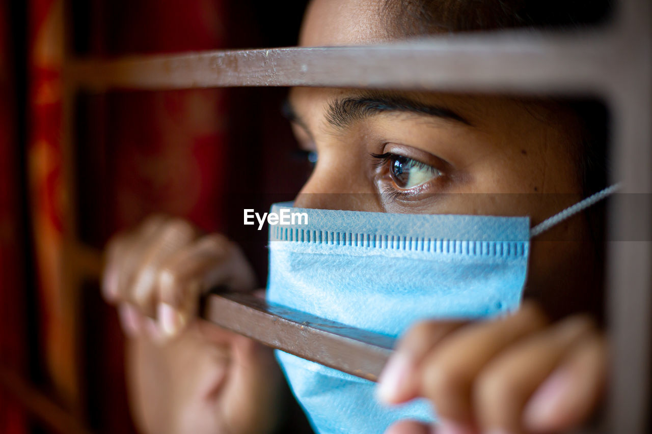 Close-up of woman wearing mask looking through window