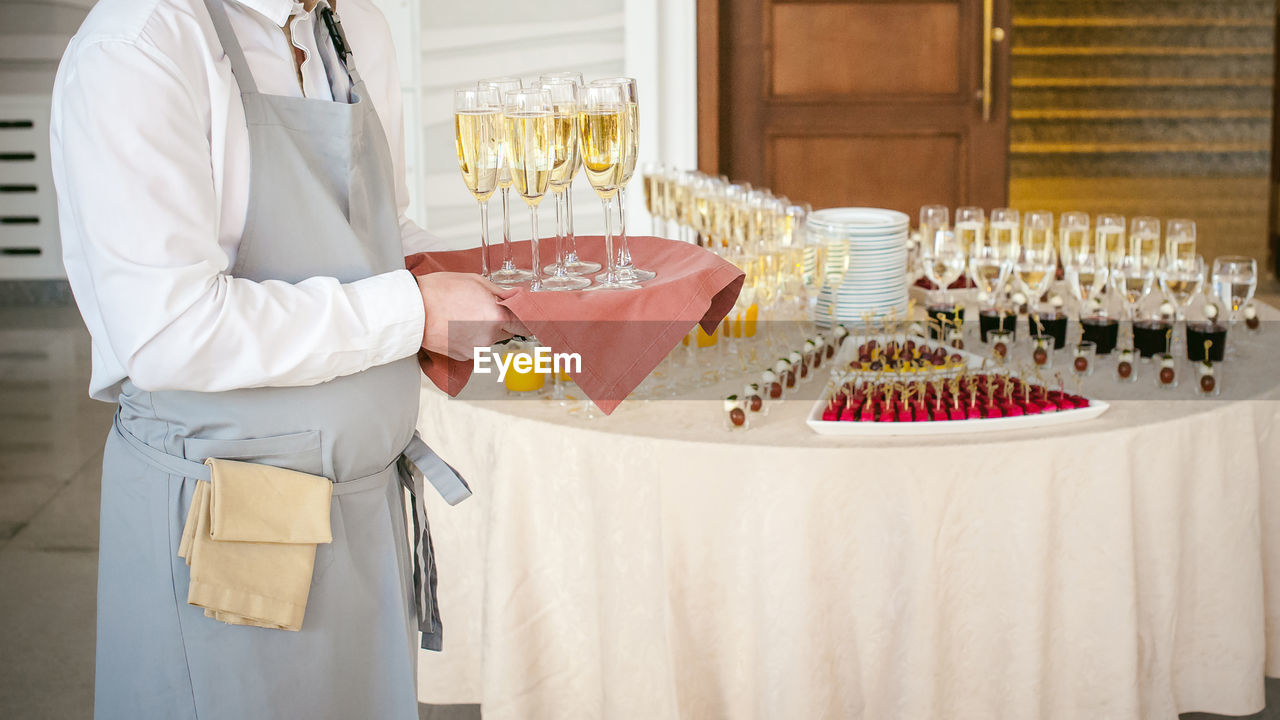 Midsection of waiter carrying white wine by tables in restaurant