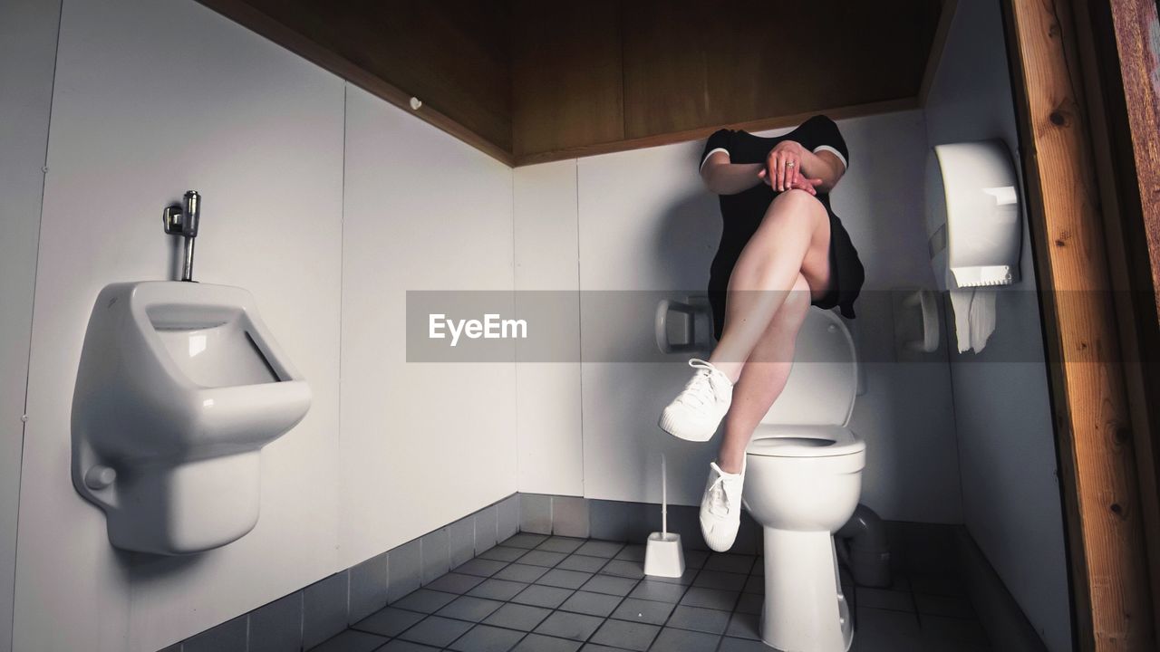 Woman sitting over commode at public toilet