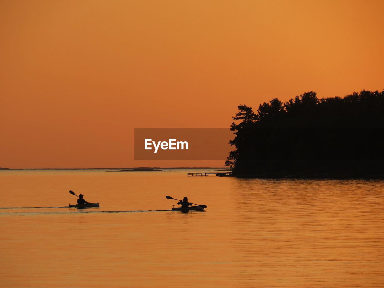 Silhouette people in boat on sea against orange sky during sunset