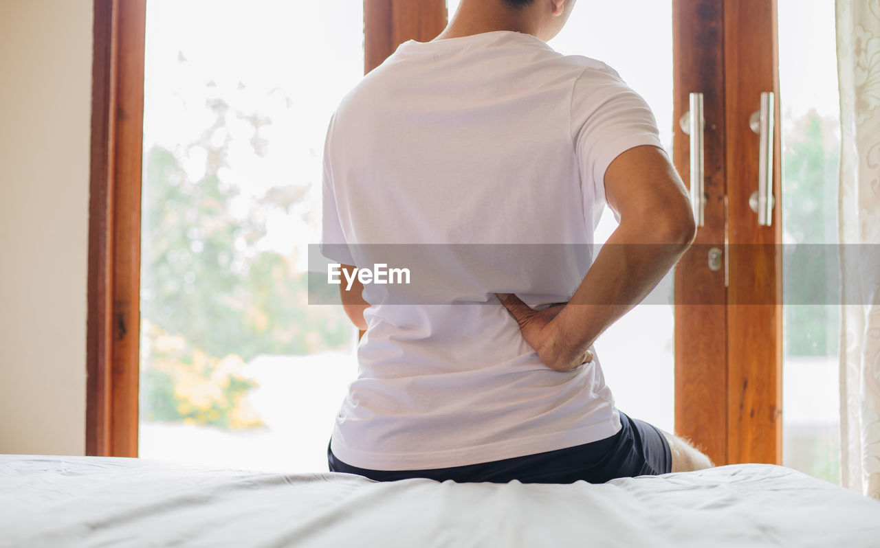 REAR VIEW OF MAN STANDING ON BED IN BEDROOM