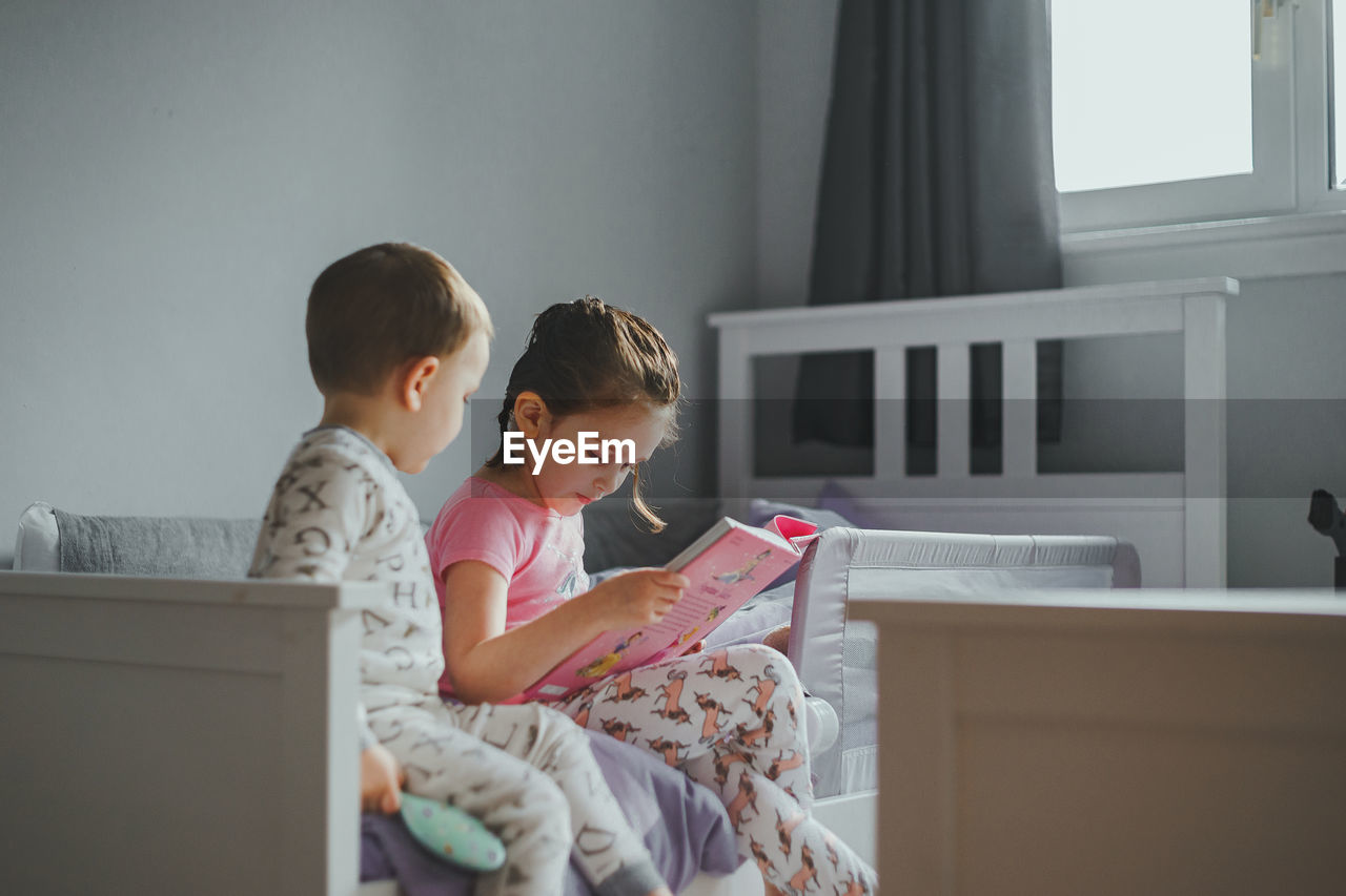 Young girl reading a story book to her brother before bedtime