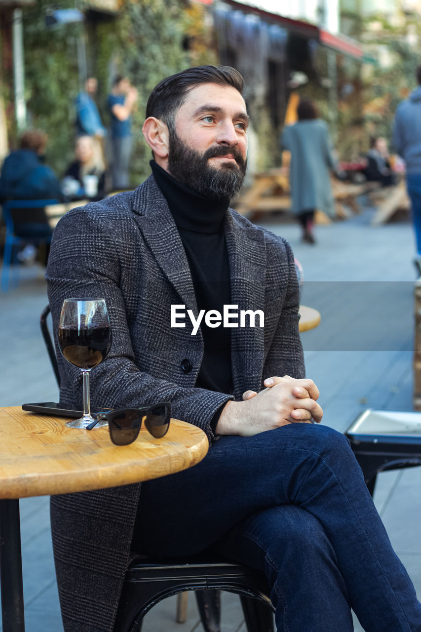 Brutal bearded middle-aged man in a street cafe with a glass of wine
