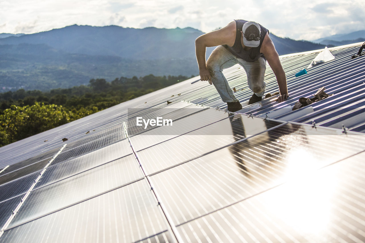 Worker carefully works to secure solar panels on roof of building.