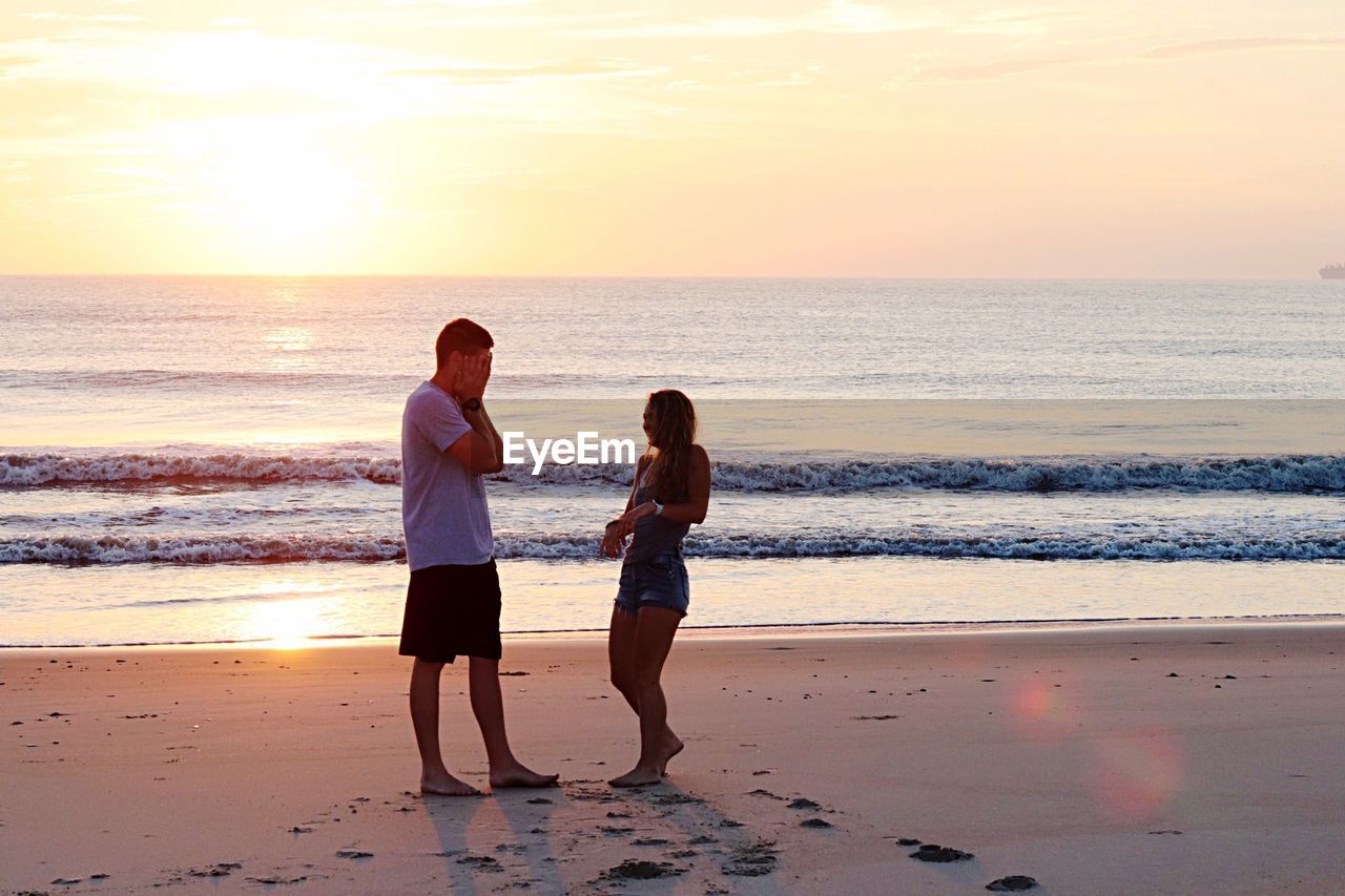 Couple standing at beach during sunset