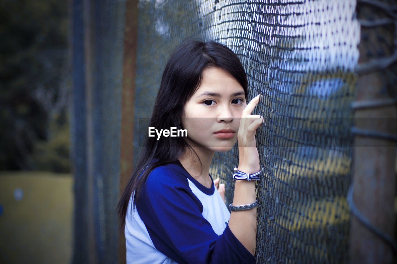 Portrait of young woman leaning on fence