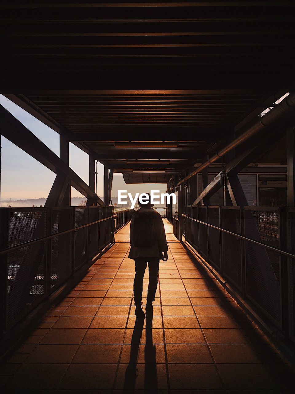 Rear view of silhouette man walking on bridge