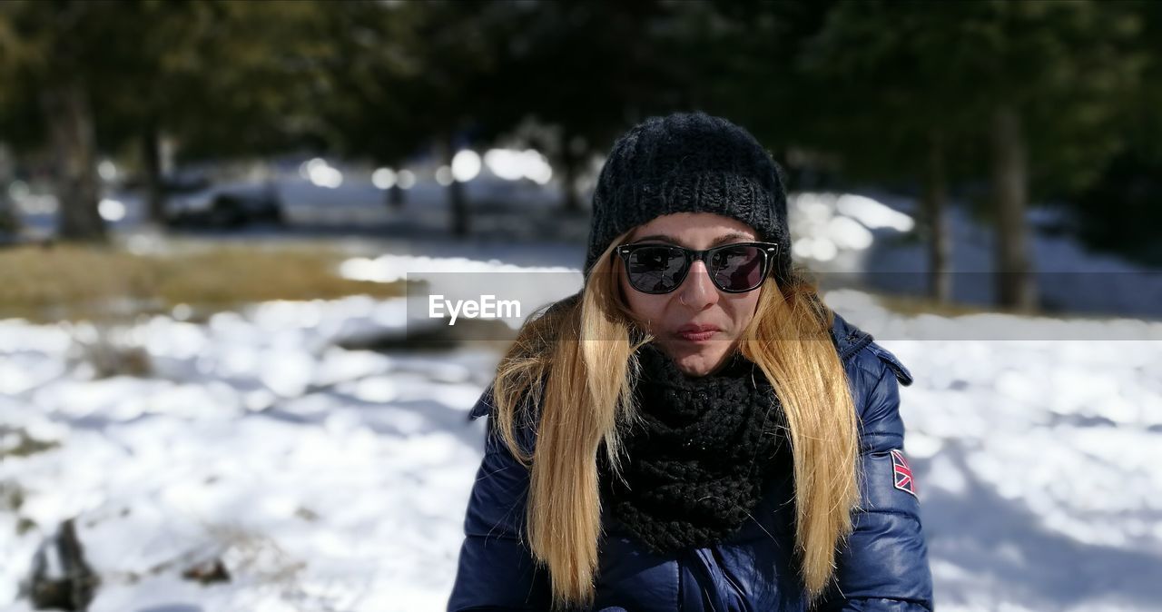 Portrait of young woman wearing sunglasses while standing on snow covered field