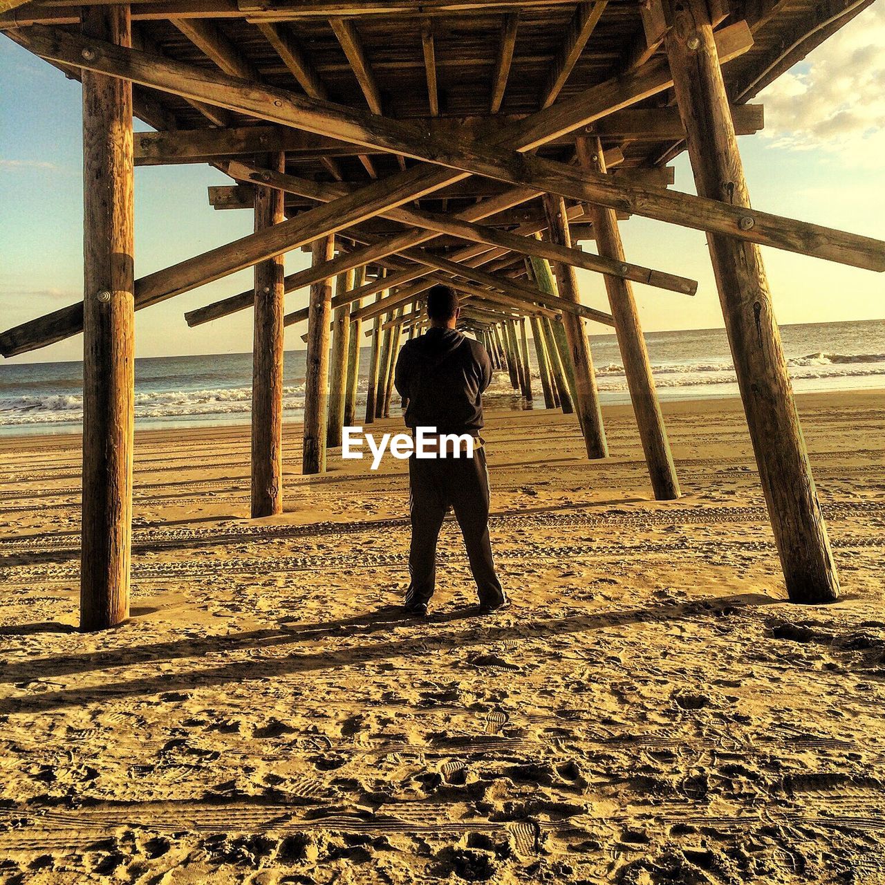 Rear view of man standing under boardwalk at beach