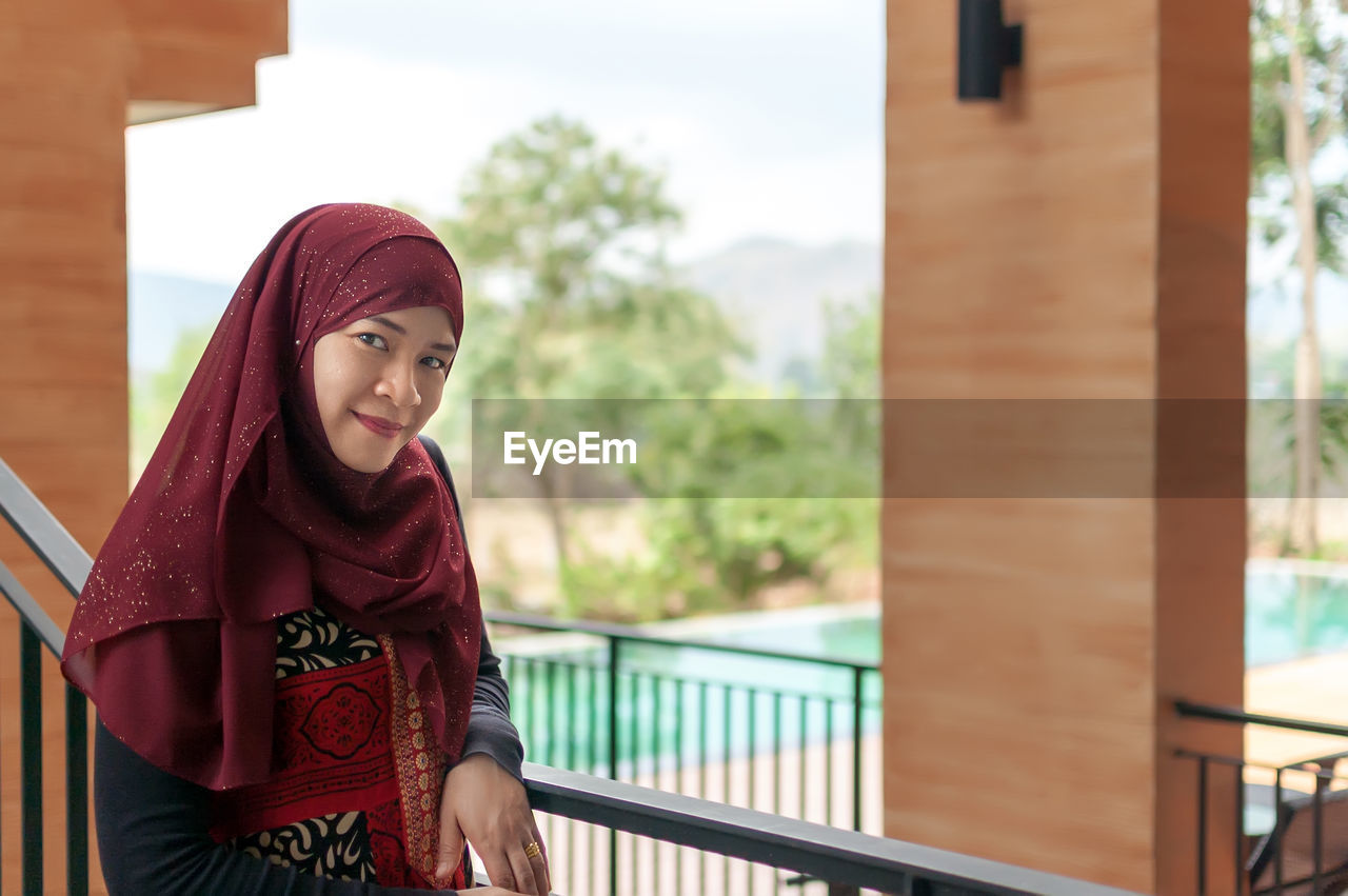 Portrait of smiling woman standing by railing