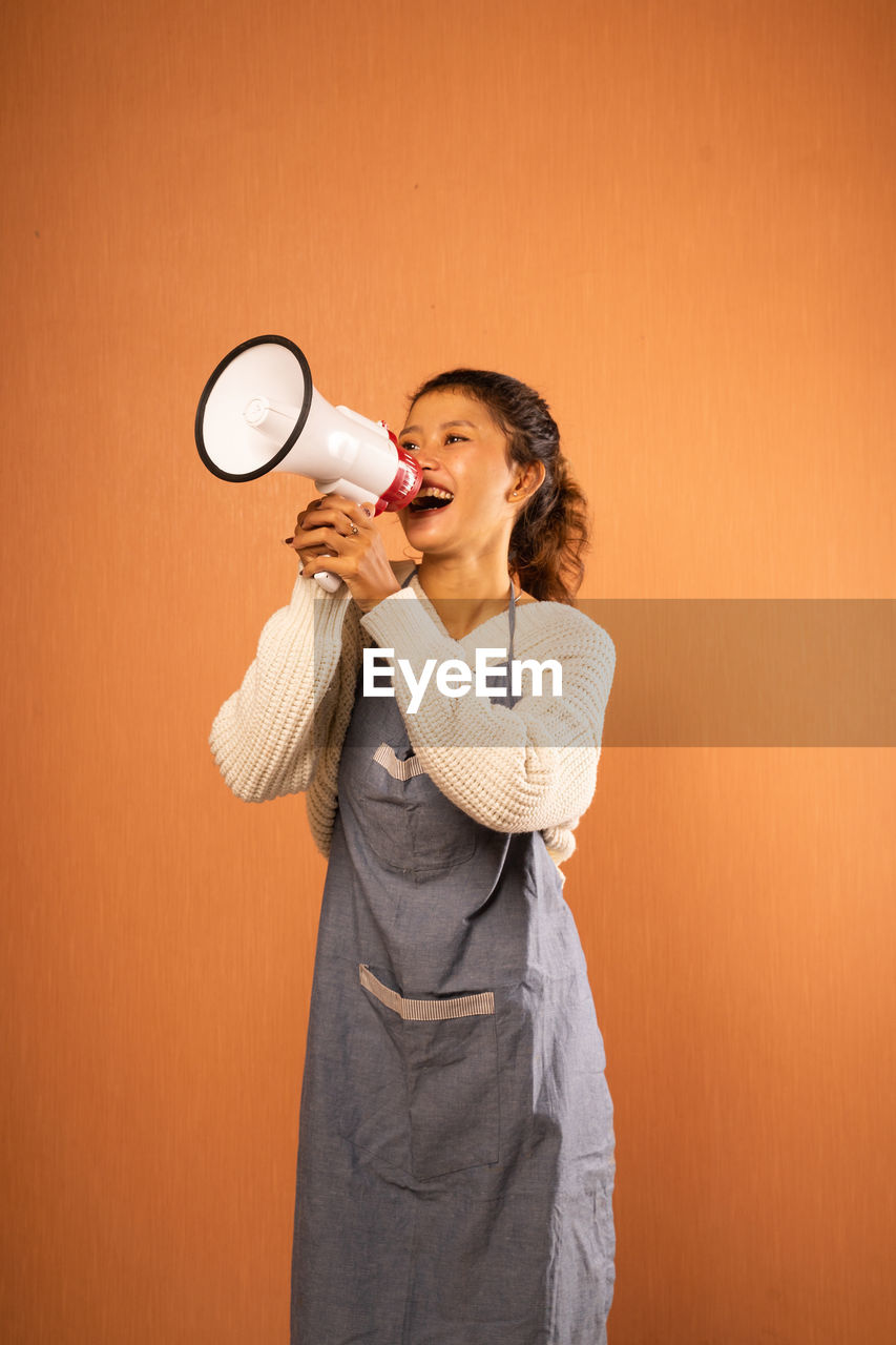 portrait of young woman drinking bottles while standing against yellow background