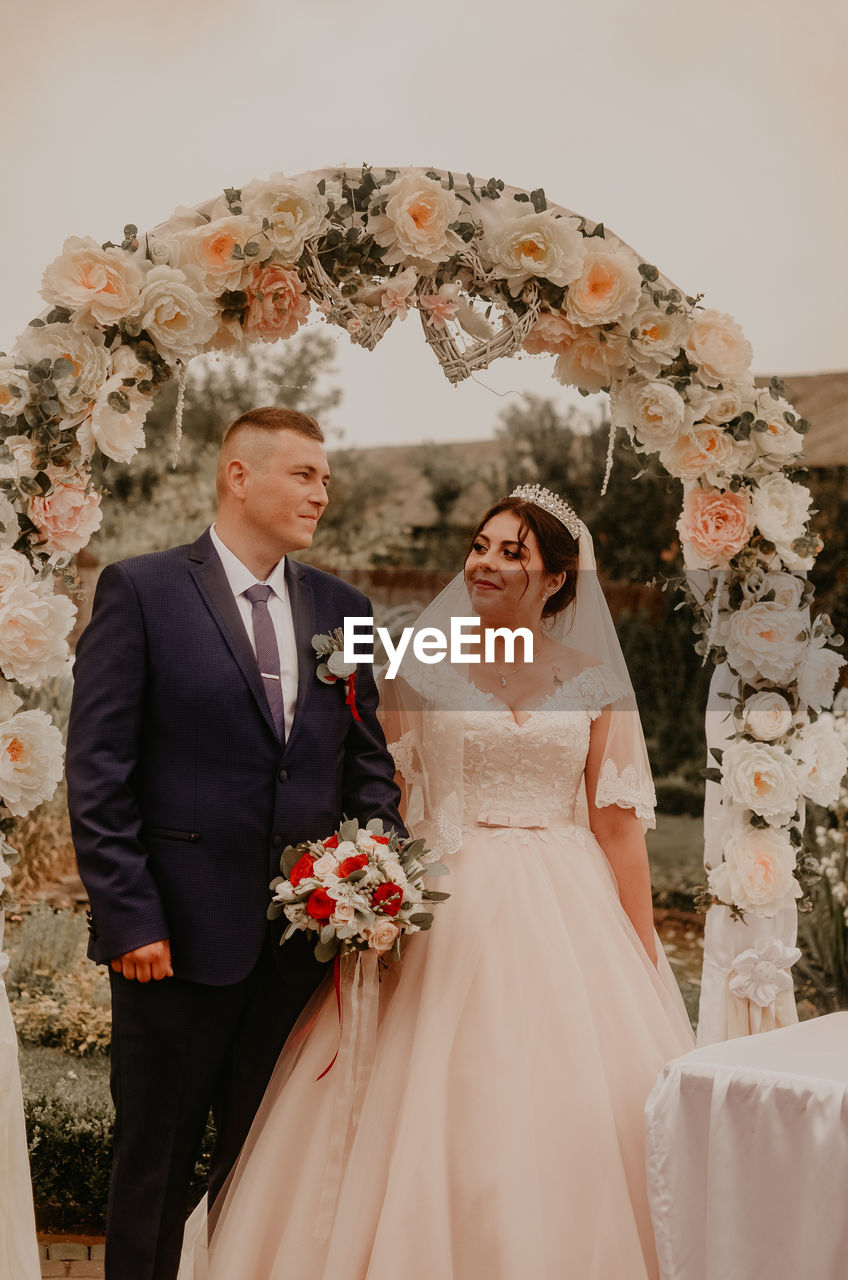 portrait of bride and bridegroom standing against white wall