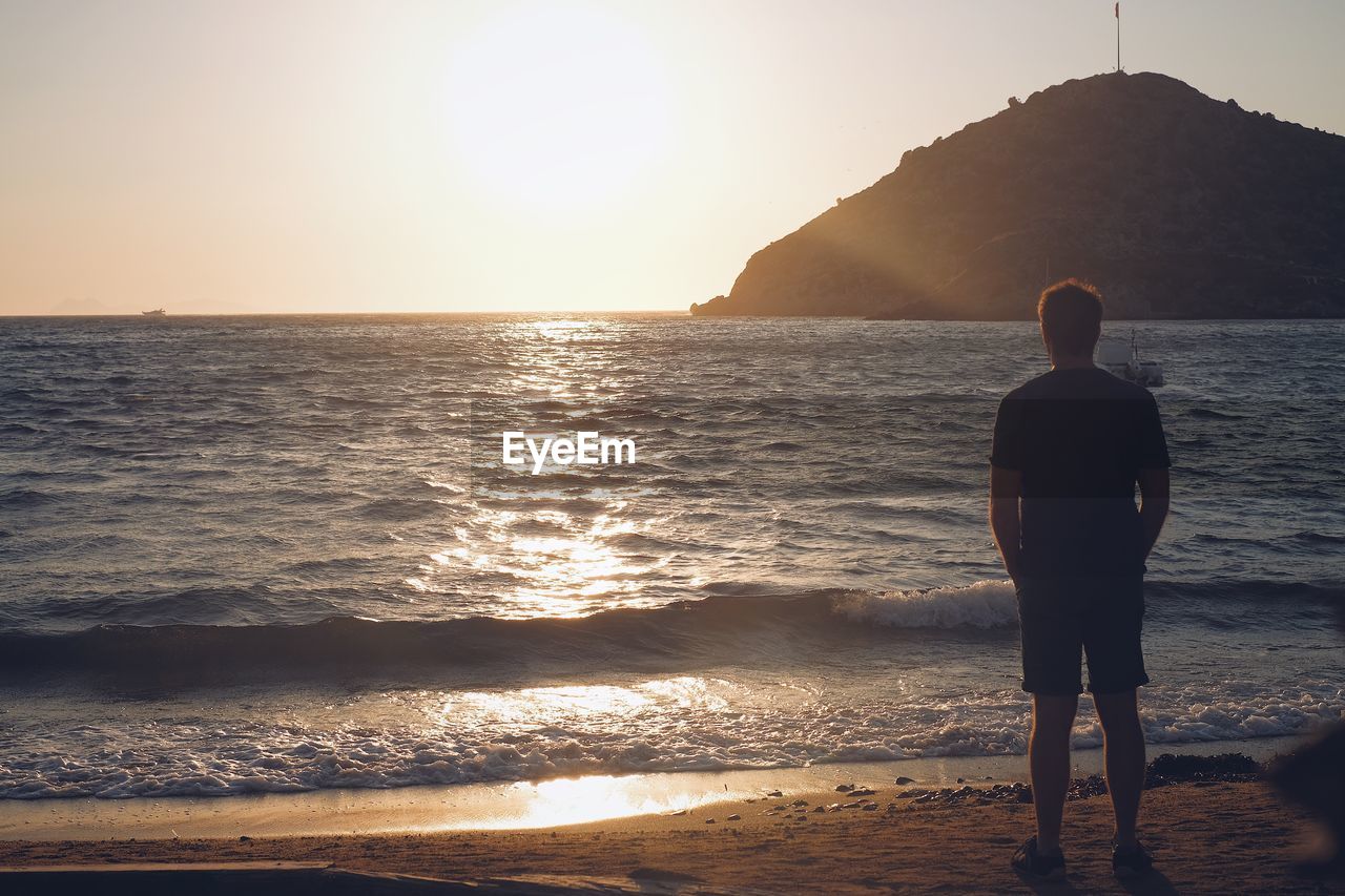 Rear view of man looking at sea during sunset