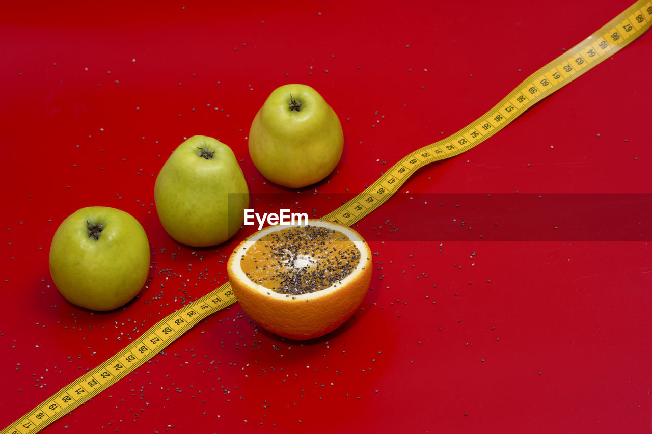 Close-up of fruits and tape measure over red background