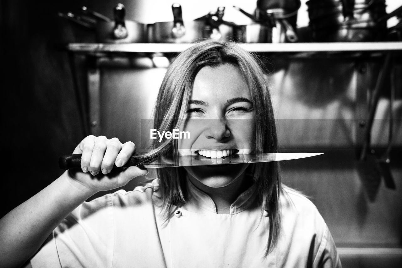 PORTRAIT OF YOUNG WOMAN HOLDING CAMERA WHILE STANDING IN KITCHEN