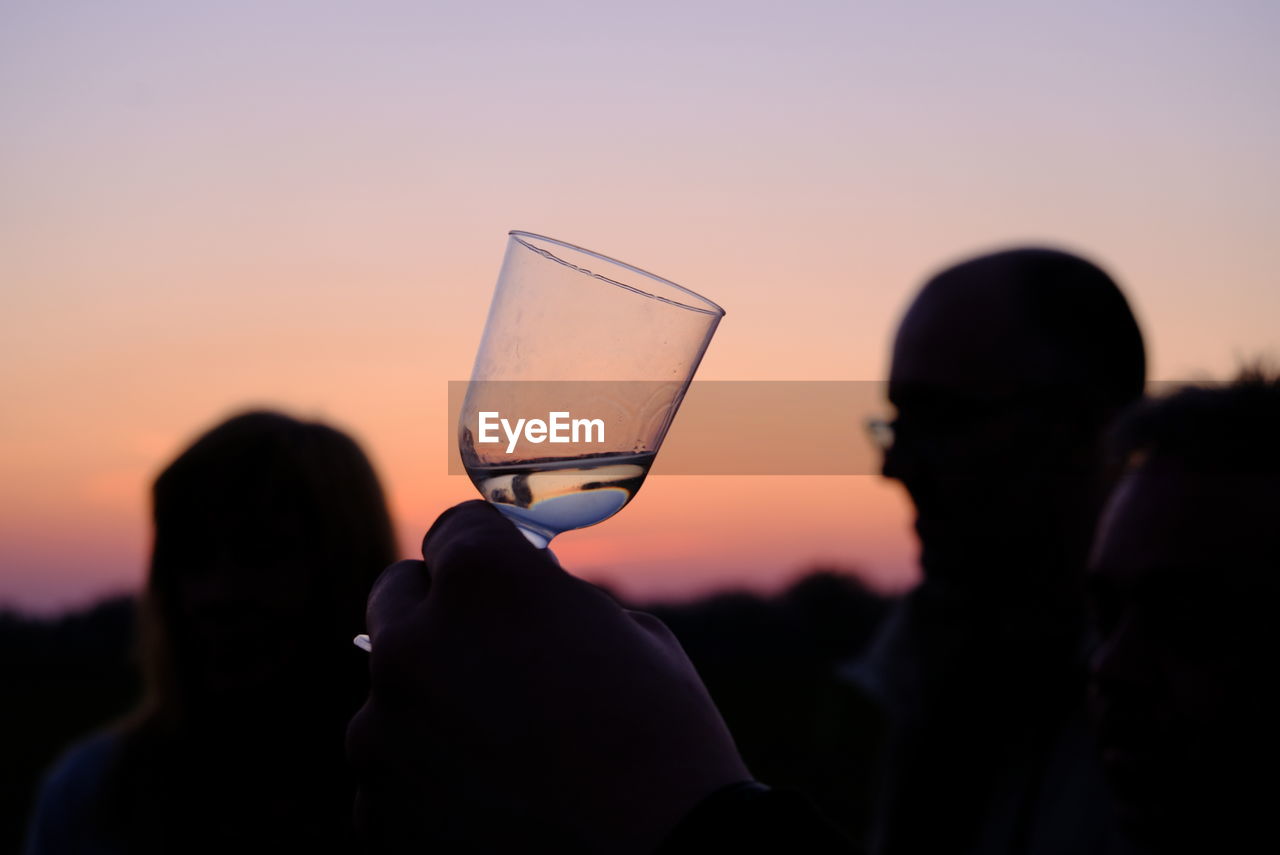 Close-up of silhouette man drinking glass against sunset sky