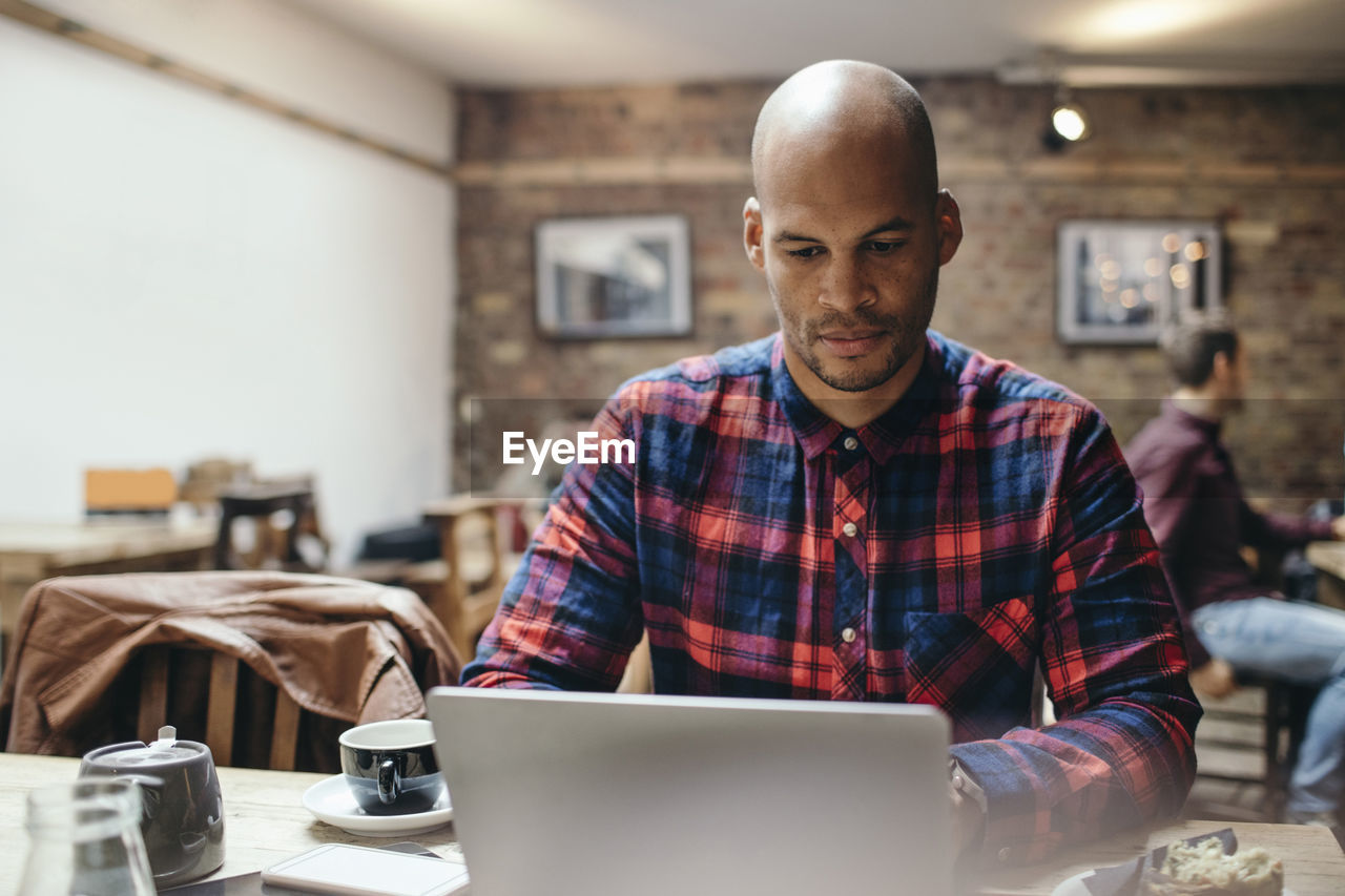 Mid adult man using laptop at table in coffee shop