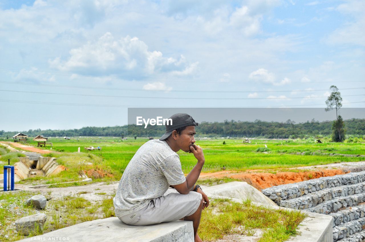 Side view of thoughtful man sitting on field against sky