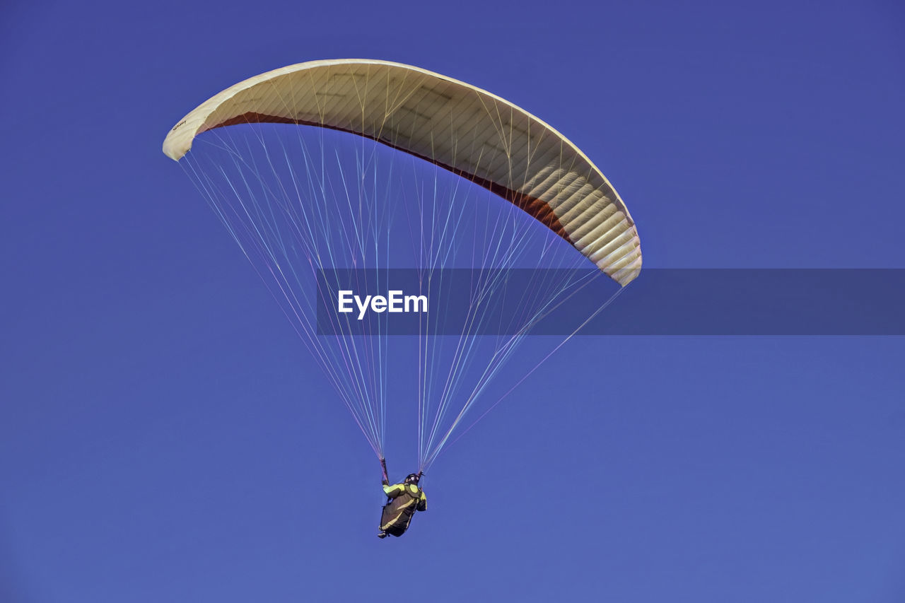 Low angle view of person paragliding against clear blue sky on sunny day