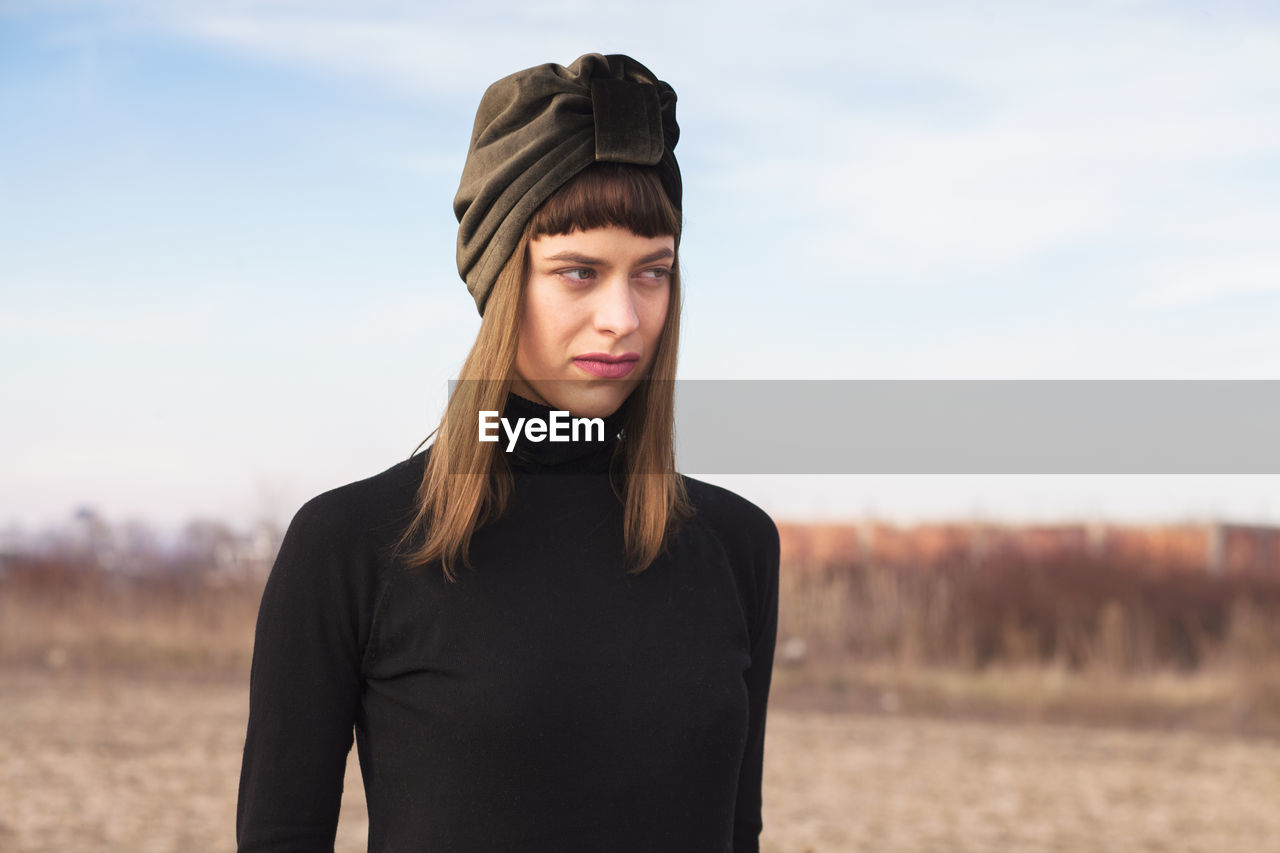 Beautiful woman looking away while standing on field against sky