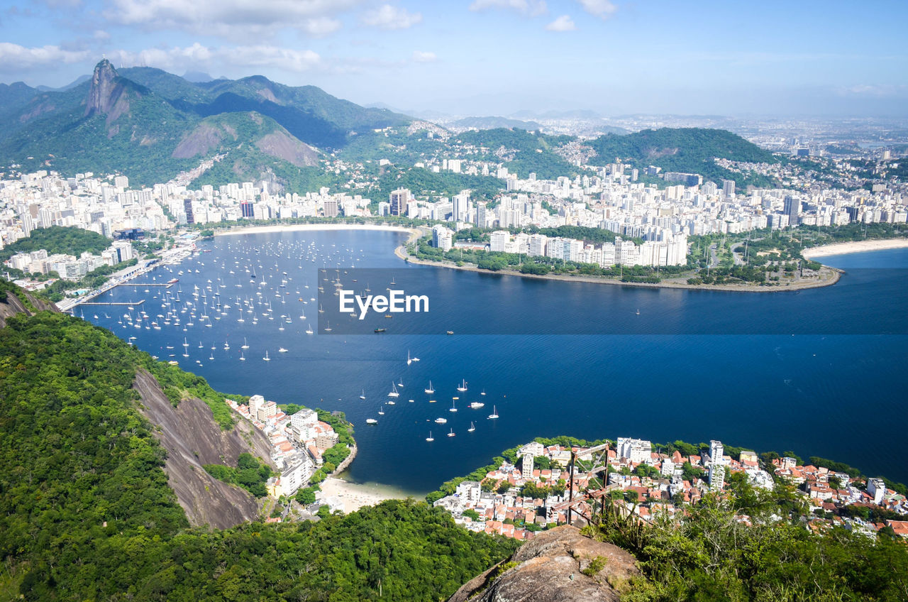 HIGH ANGLE VIEW OF SEA BY CITYSCAPE AGAINST SKY