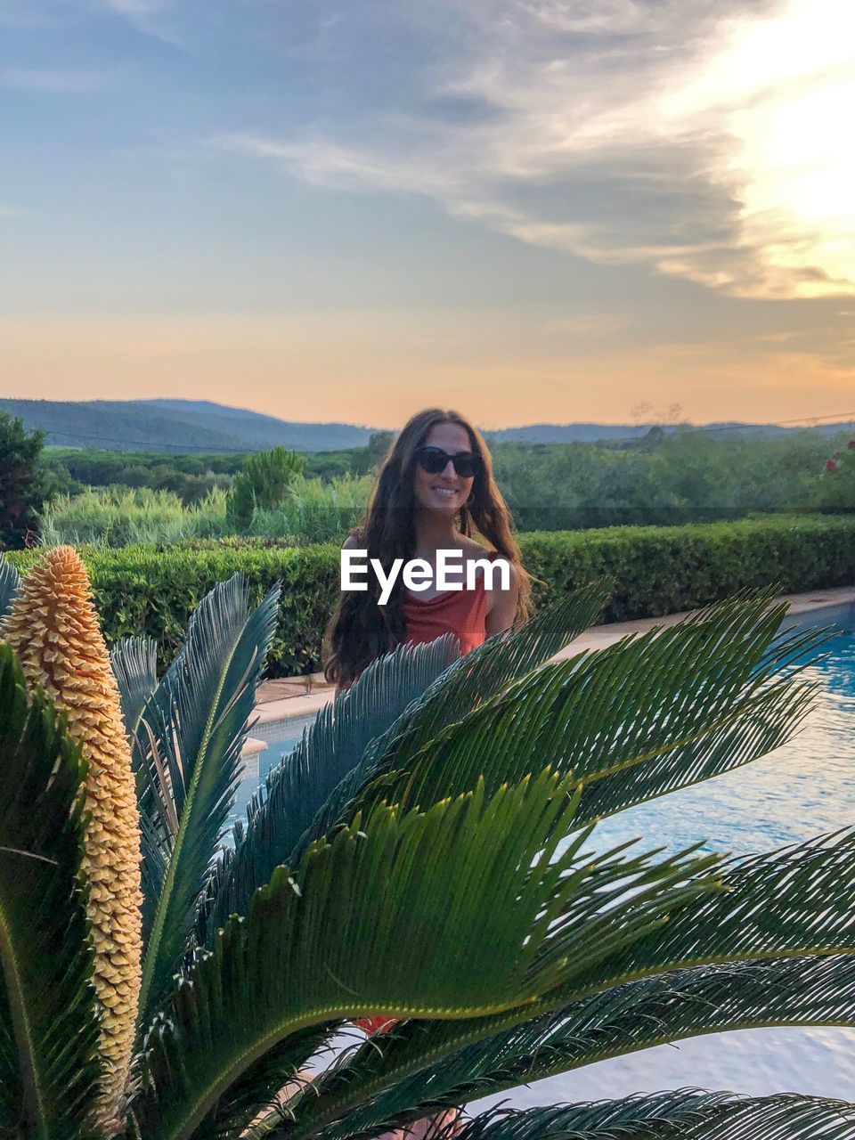Smiling woman standing at swimming pool against sky