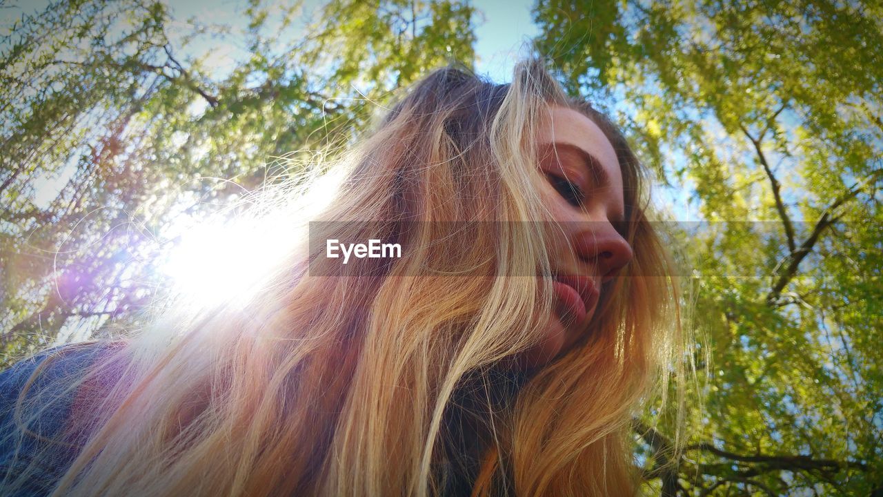 Low angle view of thoughtful young woman standing against trees