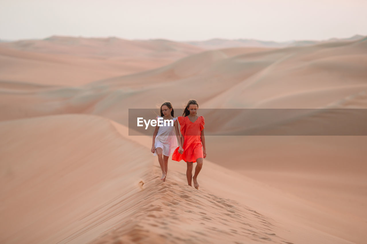 Sisters walking on sand dunes at desert
